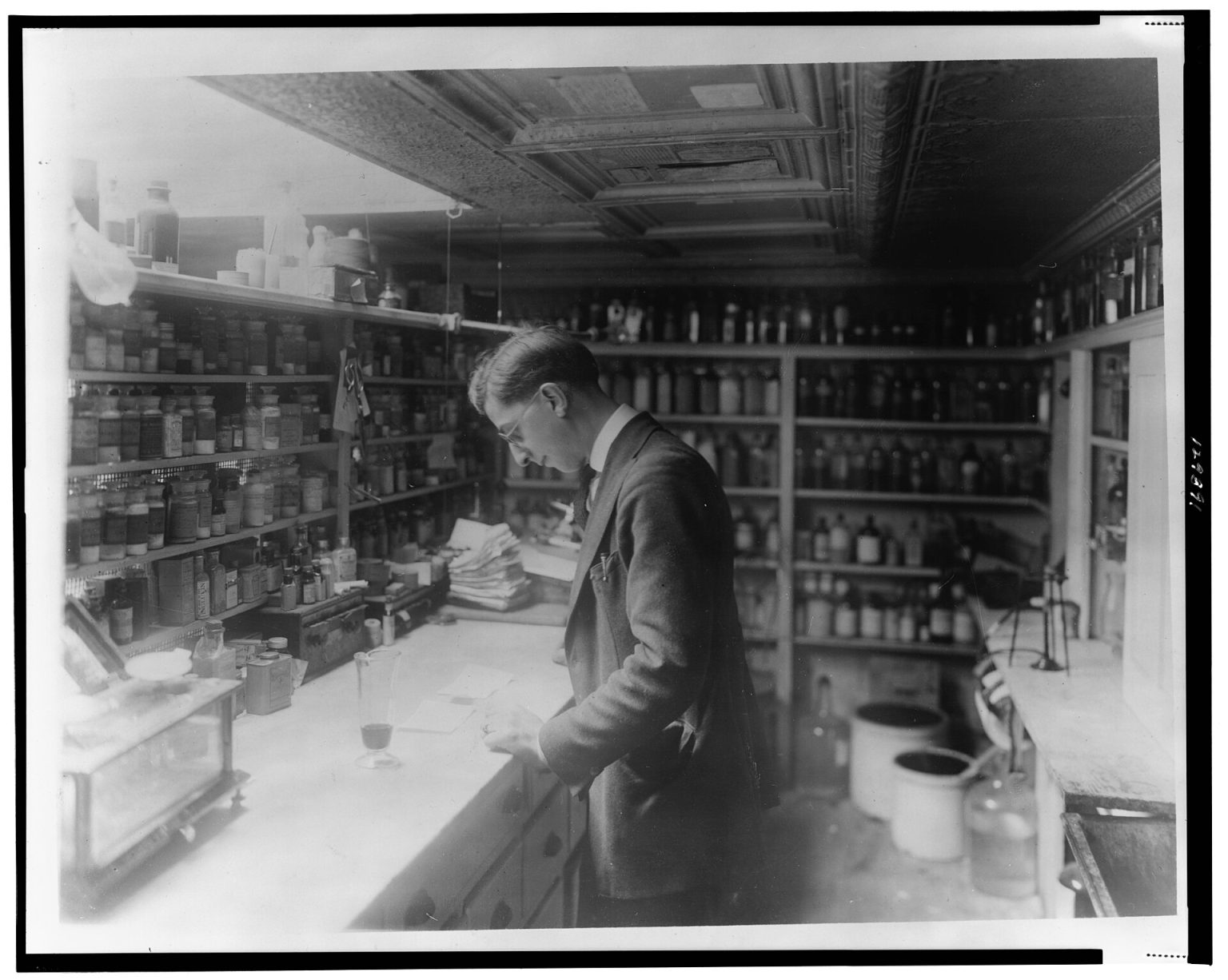 Pharmacist at People's Drug Store, No. 5, 8th and H Streets, N.E., Washington, D.C., looking at prescriptions(?) on the counter in room lined with she